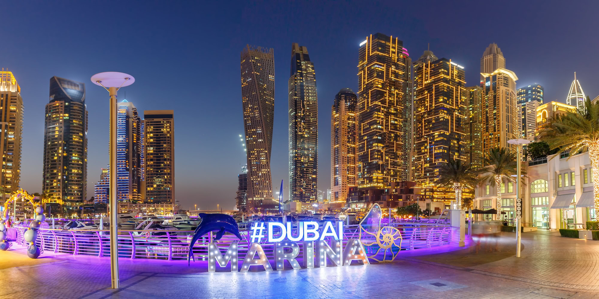 Tourists on a Dubai beachfront promenade with city skyline hotels